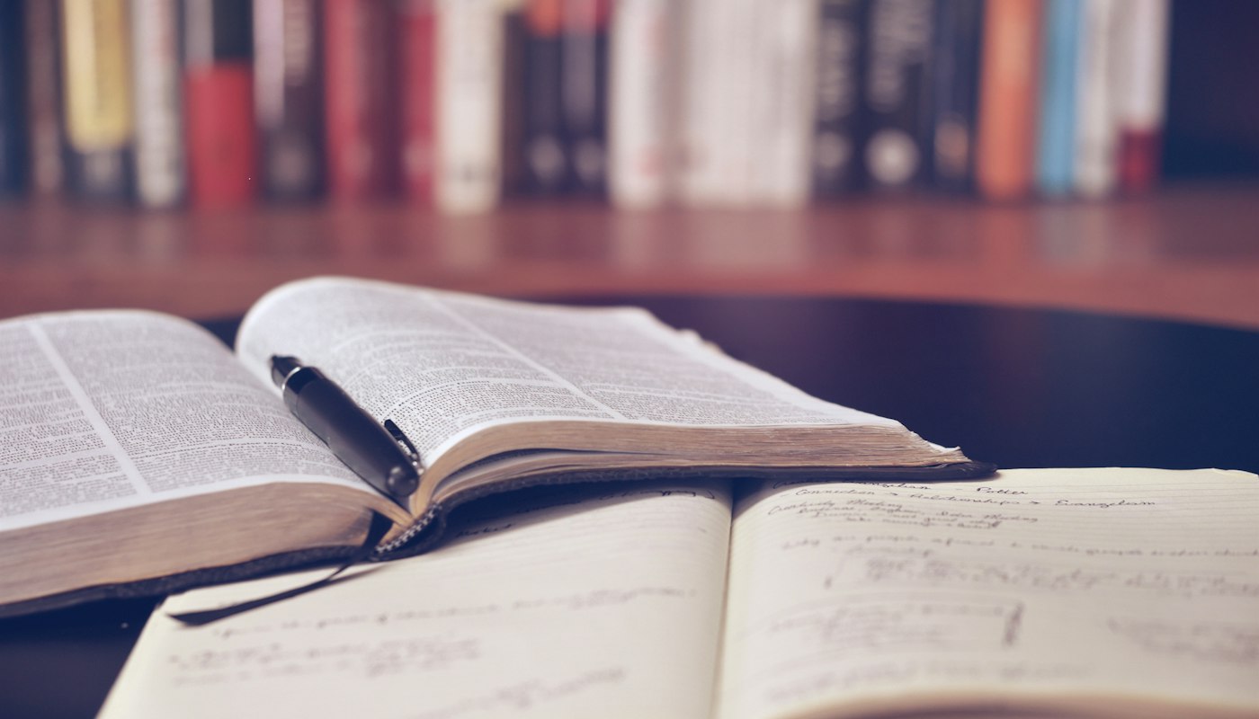 Livro aberto e caderno de anotações sobre a mesa de estudos